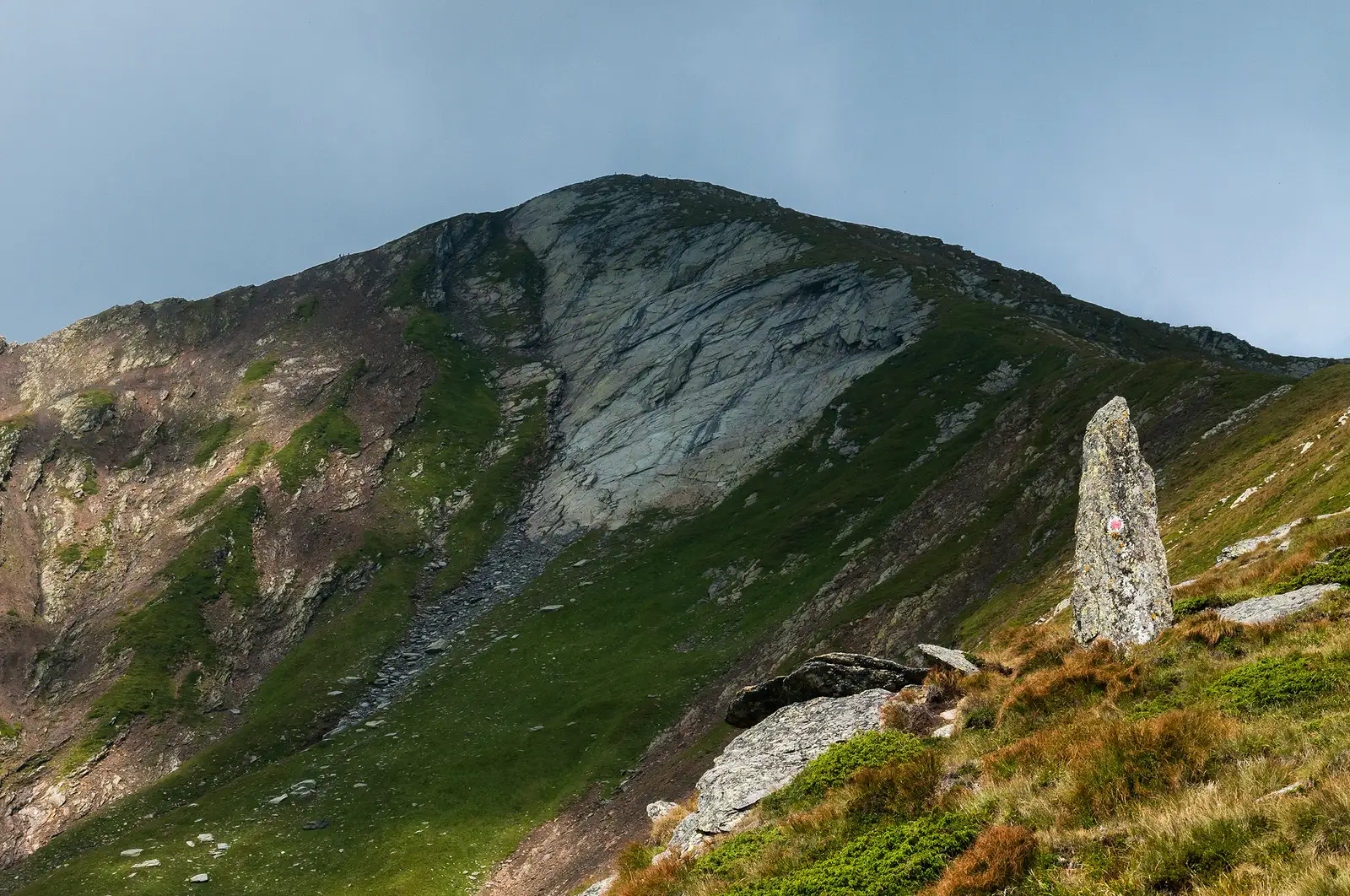  Un fel de ”ac al Cleopatrei” dar minuscul pe care se află aplicat marcajul punct roșu. În fundal Vf. Lespezi.